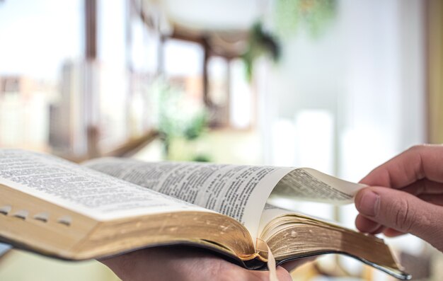 Un hombre sostiene una Biblia y lee un libro en la terraza. Hora de la mañana. De cerca.