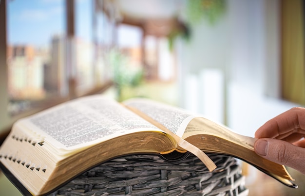 Un hombre sostiene una Biblia y lee un libro en la terraza. Hora de la mañana. De cerca.