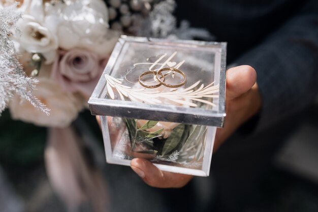 El hombre sostiene una pequeña caja transparente con dos anillos de boda