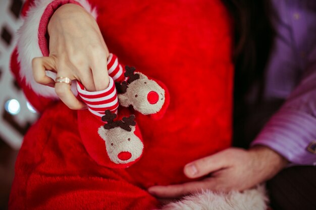 El hombre sostiene pequeños zapatos rojos en el vientre de la mujer