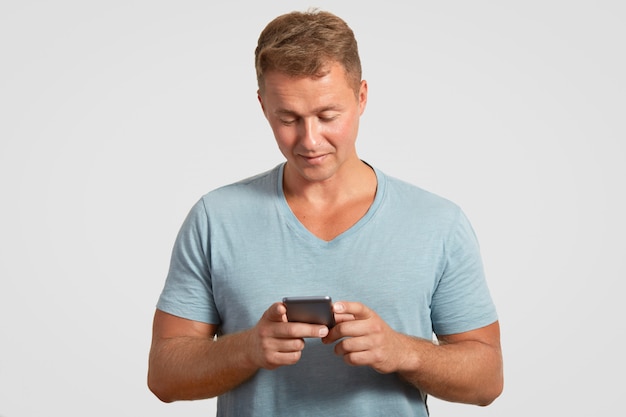 El hombre sostiene un teléfono inteligente moderno, envía mensajes de texto, revisa su casilla de correo electrónico y está conectado a Internet inalámbrico
