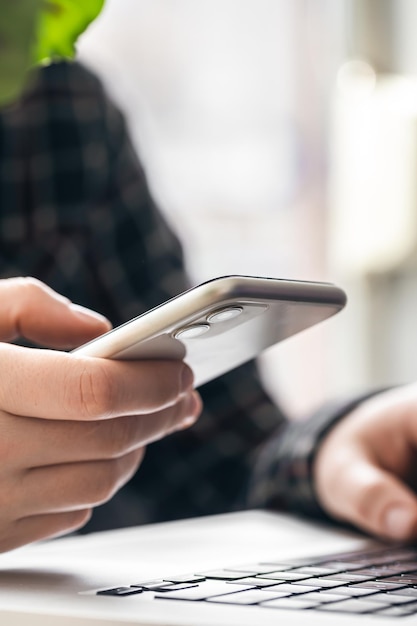 Un hombre sostiene un teléfono inteligente y trabaja en una computadora portátil.