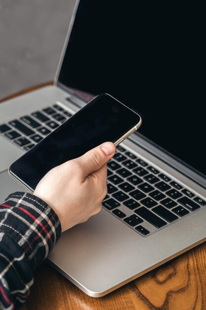 Un hombre sostiene un teléfono inteligente y trabaja en una computadora portátil.