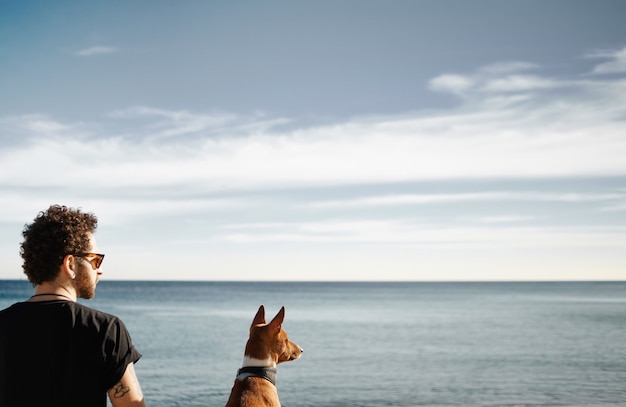 Foto gratuita hombre y su perro en la playa admirando el mar