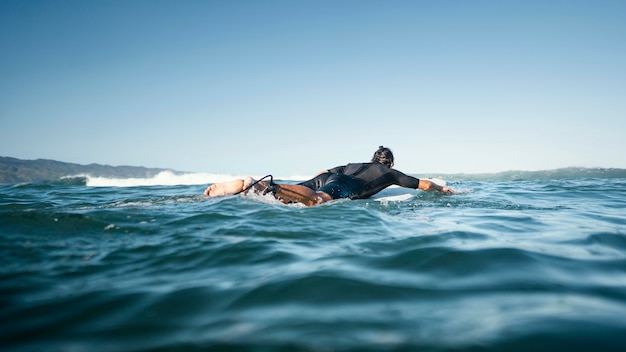 Hombre en su tabla de surf nadar tiro largo