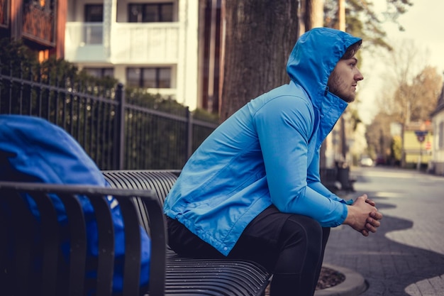 Un hombre con una sudadera con capucha azul descansando en un banco.