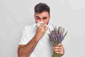 Foto gratuita el hombre se suena la nariz con un pañuelo tiene estornudos y rinitis alergia a los ojos rojos lavanda hinchazón sufre de síntomas desagradables aislados en la pared blanca. concepto de enfermedad