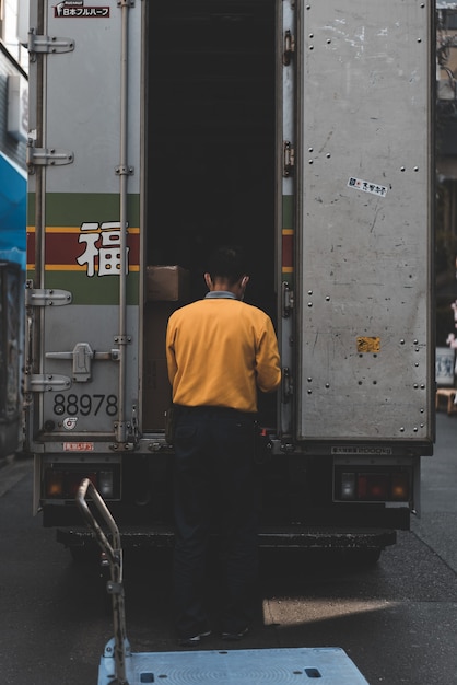 Hombre de suéter amarillo detrás de camión caja gris