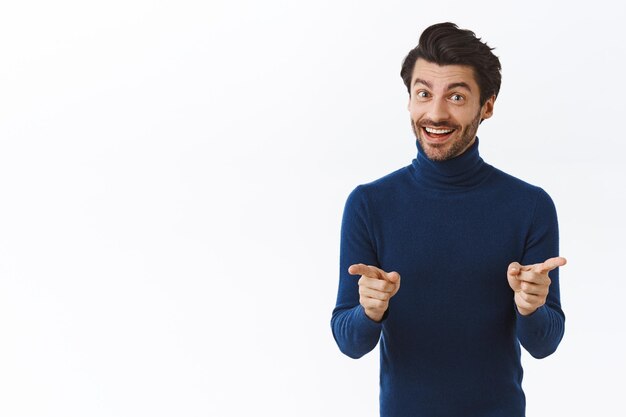 Hombre con suéter azul de cuello alto, apuntando a la cámara y sonriendo encantado, anima a los empleadores durante la reunión