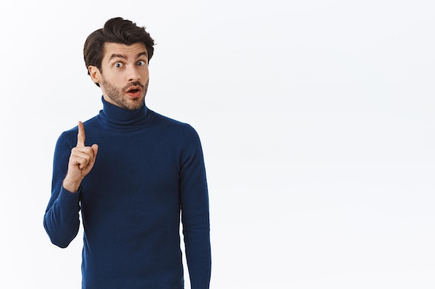hombre con suéter azul de cuello alto levanta un dedo y comparte su pensamiento, sugiere algo durante la reunión de la oficina, da un consejo o recomienda un producto