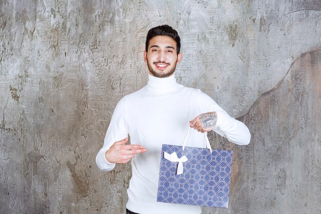 Hombre de suéter blanco sosteniendo una bolsa azul.