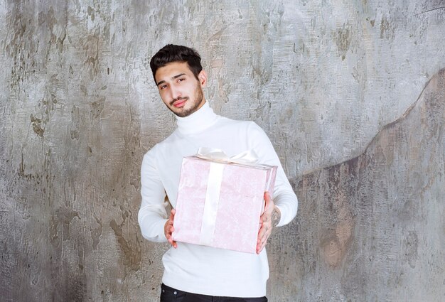 Hombre de suéter blanco sosteniendo una caja de regalo púrpura envuelta con cinta.