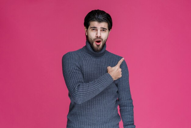 Hombre de suéter gris apuntando algo o presentando a alguien usando el dedo índice.