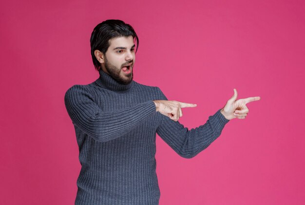 Hombre de suéter gris apuntando algo o presentando a alguien usando el dedo índice.