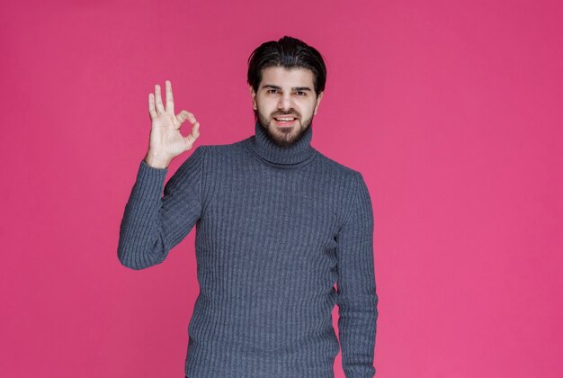 Hombre de suéter gris haciendo signo de mano positivo y bueno.