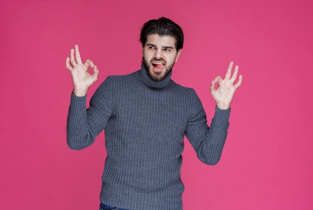 Hombre de suéter gris haciendo signo de mano positivo y bueno.