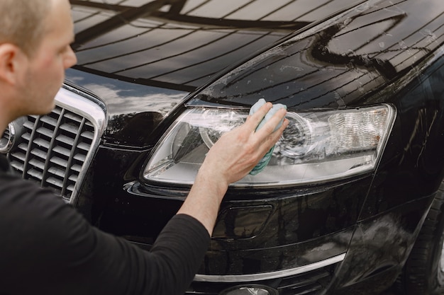 Hombre en un suéter gris limpia un automóvil en un lavadero de autos