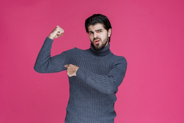 Hombre de suéter gris mostrando el músculo del brazo.