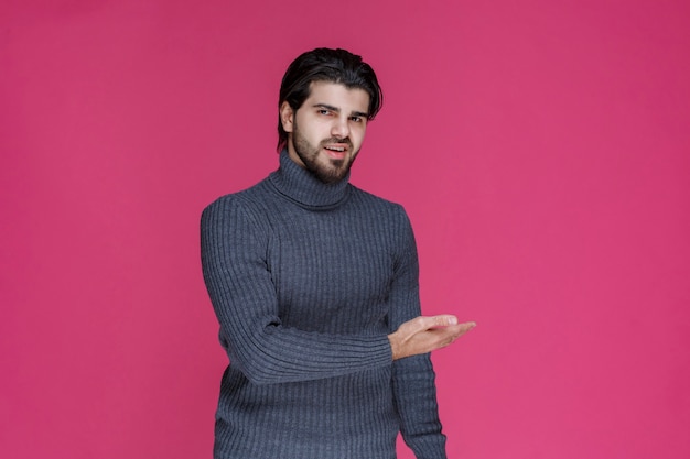 Hombre de suéter gris presentando o saludando a alguien con mucha energía y entusiasmo.