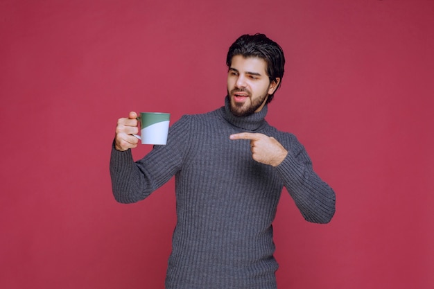 Hombre de suéter gris sosteniendo una taza de café y apuntando.