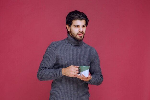 Hombre de suéter gris sosteniendo una taza de café en la mano.