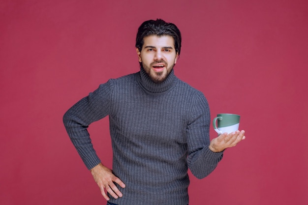 Hombre de suéter gris sosteniendo una taza de café en la mano.