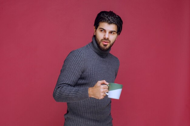 Hombre de suéter gris sosteniendo una taza de café en la mano.