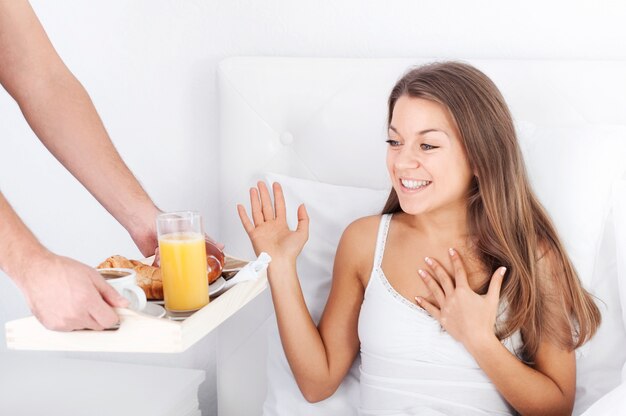 Hombre sujetando la bandeja del desayuno a la mujer en la cama