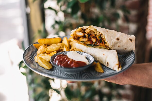 Hombre sujetando burrito de pollo servido con papas fritas mayonesa y ketchup