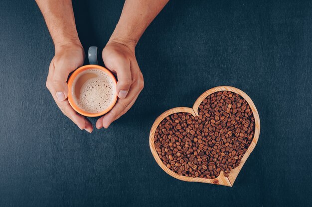 Hombre sujetando café con granos de café en un recipiente en forma de corazón sobre negro