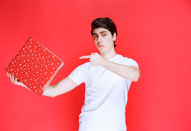 Hombre sujetando una caja de regalo roja y apuntando a ella