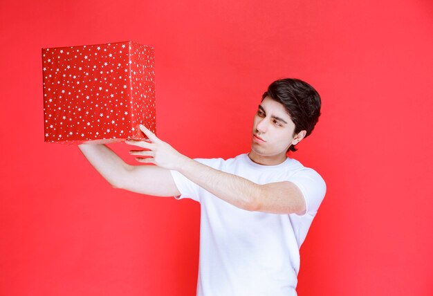 Hombre sujetando una caja de regalo roja y verificándola