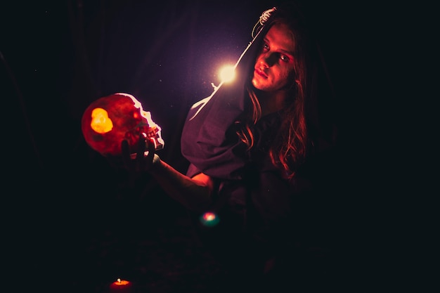 Foto gratuita hombre sujetando una calavera en la oscuridad y mirando a cámara