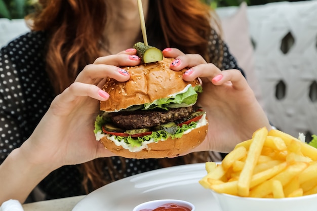 Foto gratuita hombre sujetando carne hamburguesa lechuga tomate pepino cebolla papas fritas vista lateral