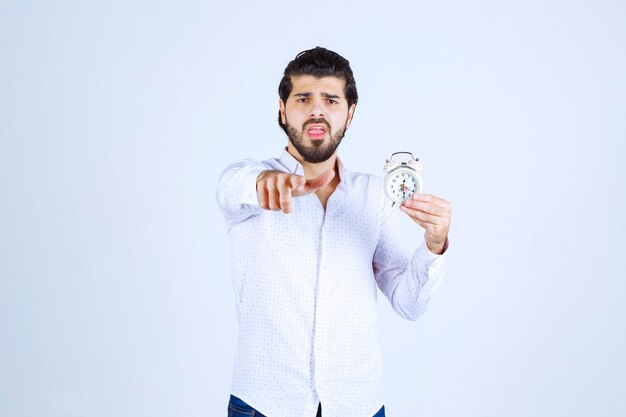 Hombre sujetando un despertador y apuntando hacia adelante