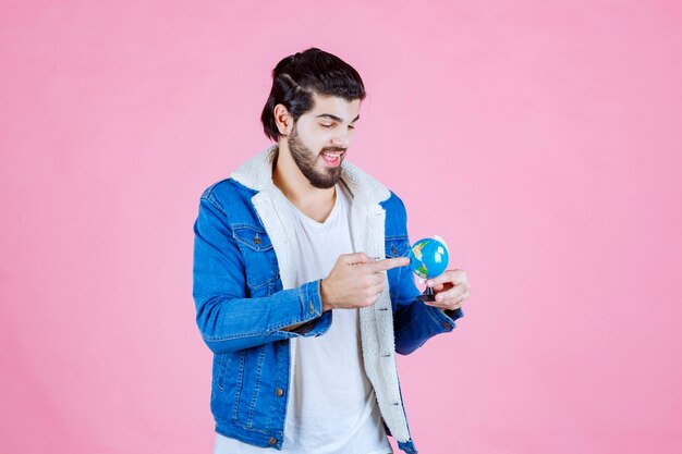 Hombre sujetando un globo terráqueo y tratando de encontrar una ubicación