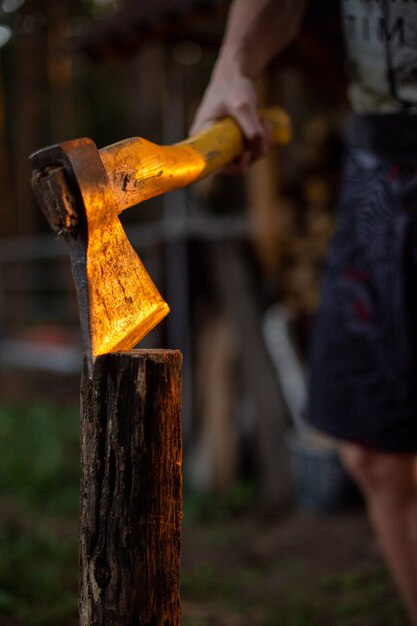 Hombre sujetando el hacha afilada en la madera cortada en el suelo