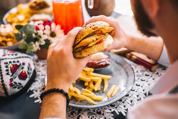 Hombre sujetando una hamburguesa de pollo servida con papas fritas y salsa