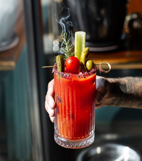 Hombre sujetando jugo de tomate adornado con apio en rama aceituna pepino en vinagre