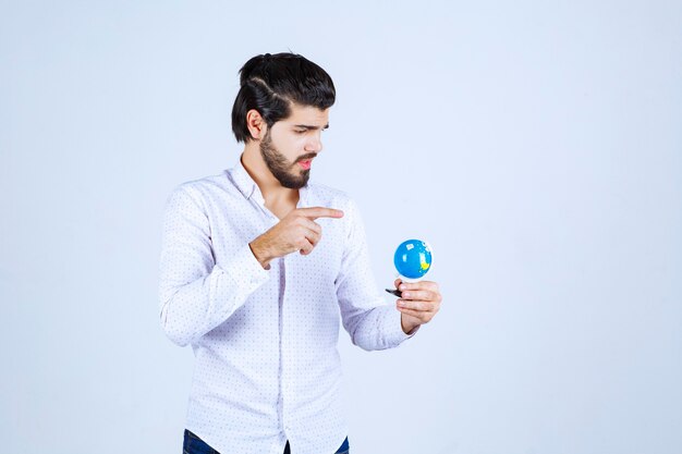 Hombre sujetando un mini globo y adivinando un lugar en él