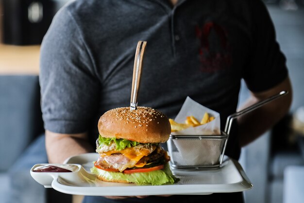 Hombre sujetando la placa con hamburguesa de ternera lechuga queso tomate pepino huevo papas fritas salsa vista lateral