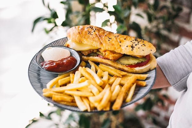 Hombre sujetando un plato de pollo doner en pan servido con papas fritas ketchup y mayonesa