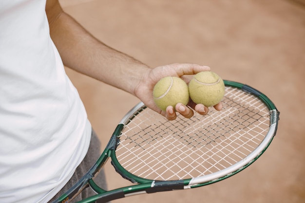 Hombre sujetando raqueta y dos pelotas de tenis