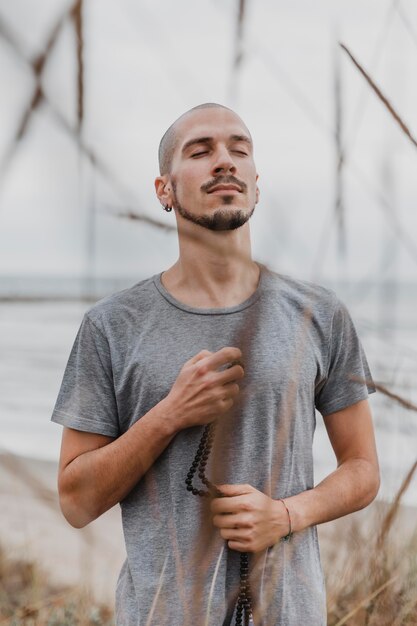 Hombre sujetando el rosario al aire libre mientras hace yoga