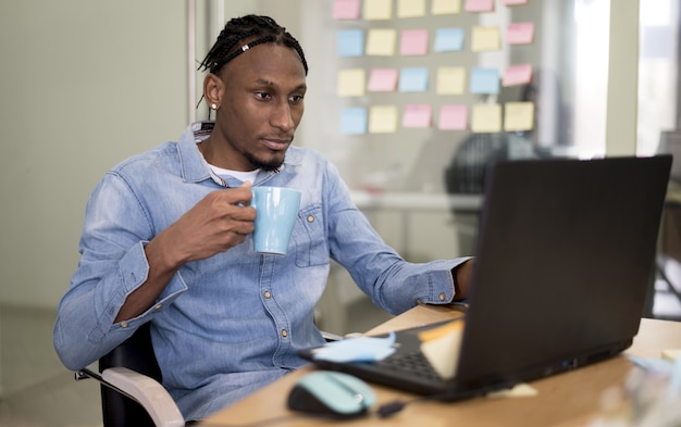 Hombre sujetando la taza y trabajando en la computadora portátil en la oficina