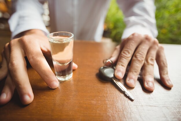Hombre sujetando un vaso de tequila shot y la llave del coche en barra de bar