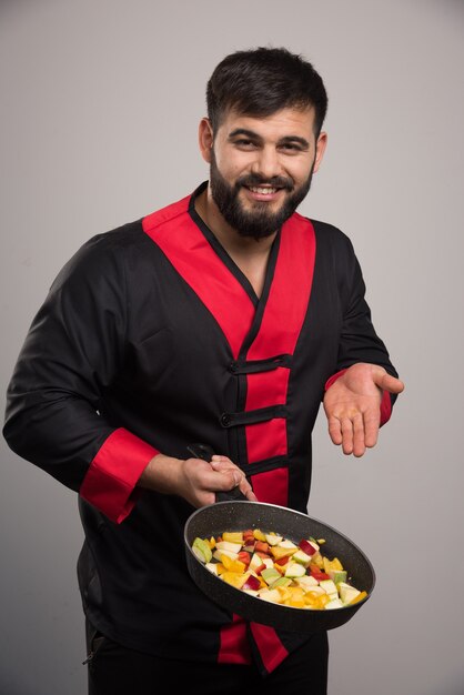 Hombre sujetando verduras en sartén oscura.