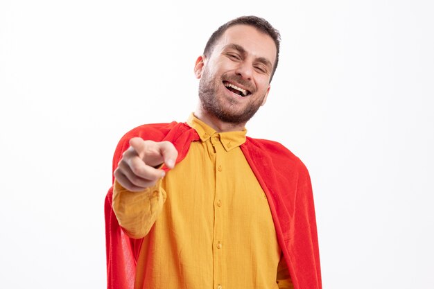 Hombre de superhéroe caucásico alegre con manto rojo mira y apunta a la cámara