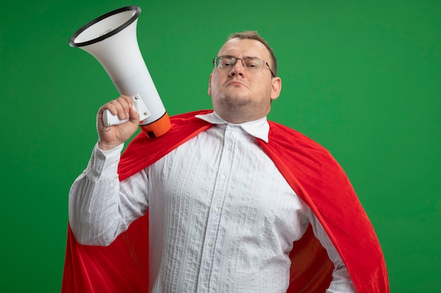 Foto gratuita hombre de superhéroe eslavo adulto confiado en capa roja con gafas sosteniendo altavoz aislado en la pared verde