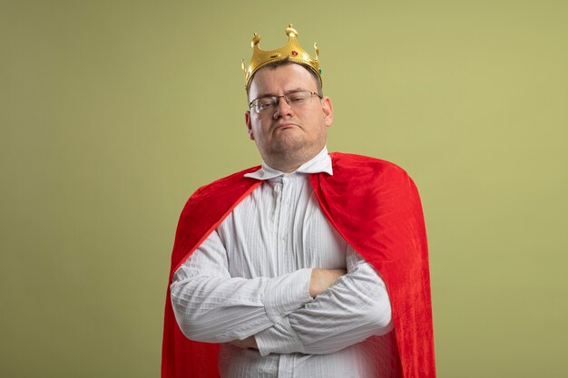 Foto gratuita hombre superhéroe eslavo adulto disgustado en capa roja con gafas y corona de pie con postura cerrada aislado en la pared verde oliva con espacio de copia